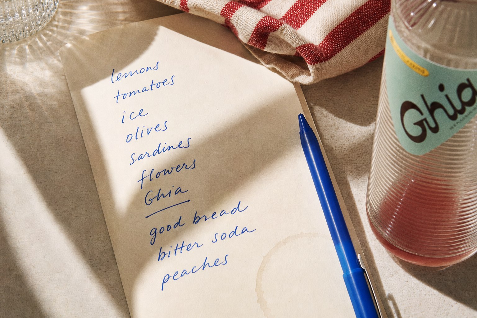 Handwritten grocery list beside Ghia bottle