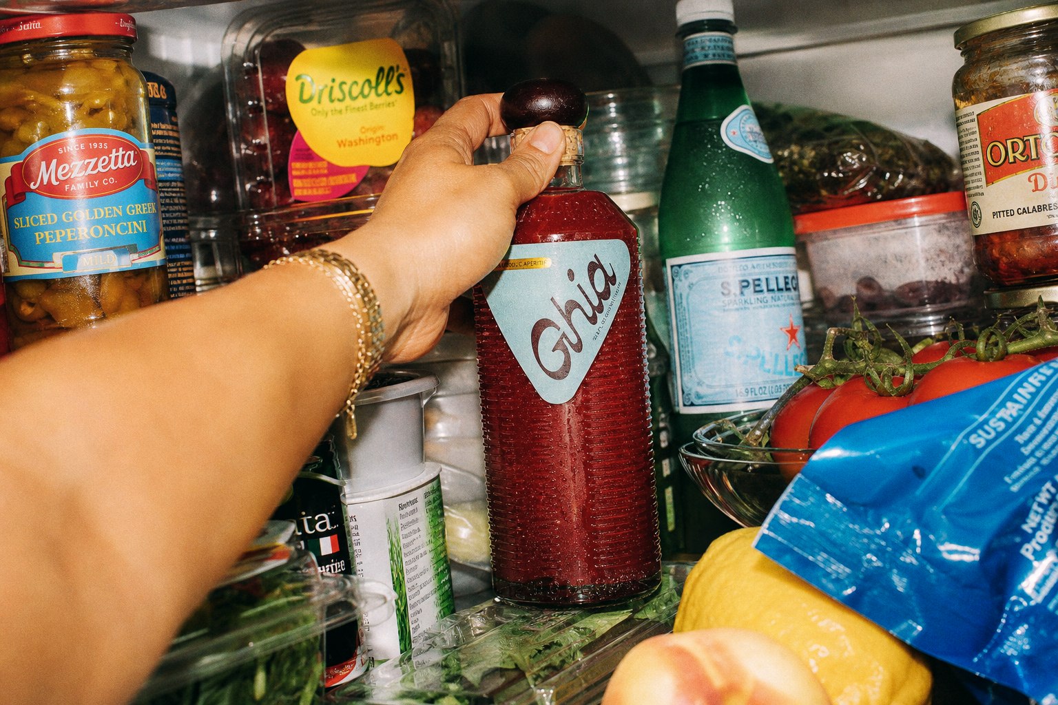 Hand reaching for chilled Ghia inside an overfilled refrigerator