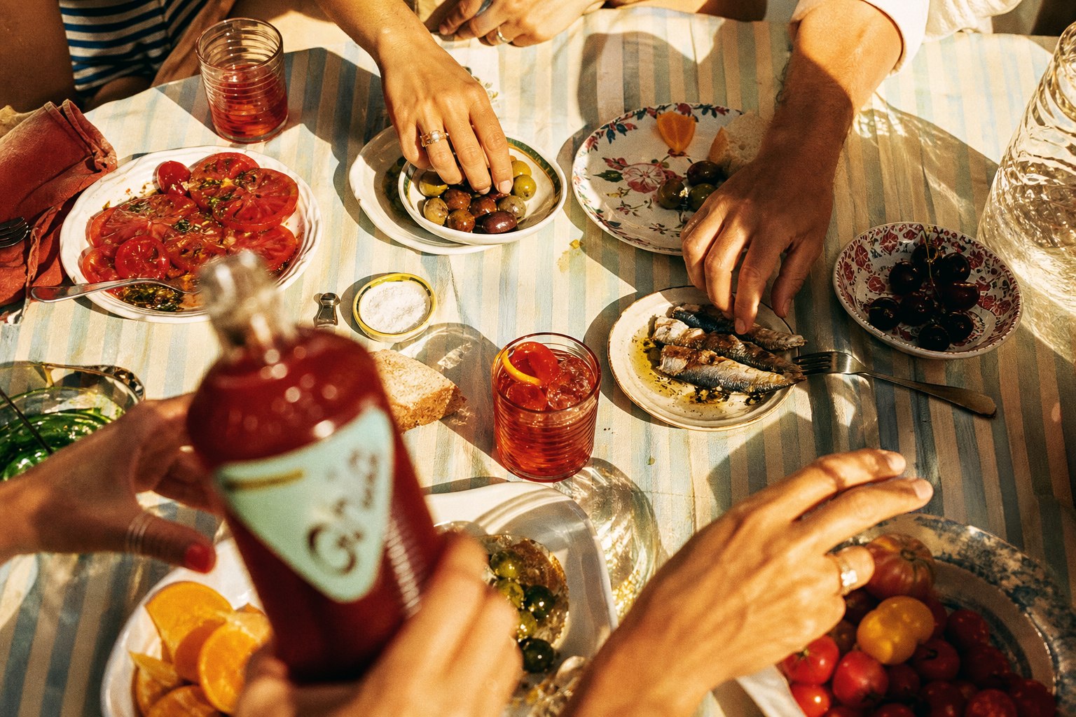 Overhead dinner table with Ghia, hands, tomatoes, and olives